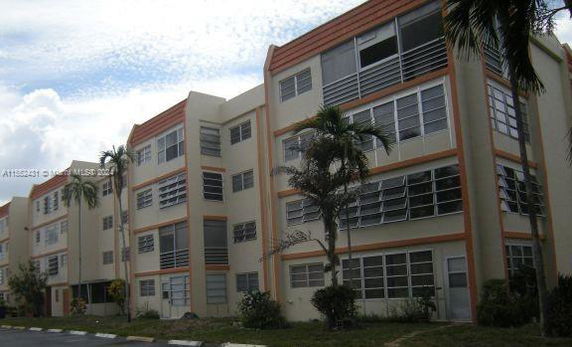 Front view of a multi-story apartment building with large windows and palm trees.
