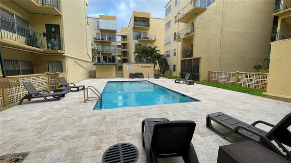 Outdoor view of an apartment complex with a swimming pool in the center and lounge chairs around it.