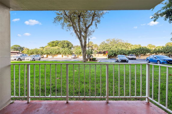 View from a balcony overlooking a grassy area and a parking lot with cars.