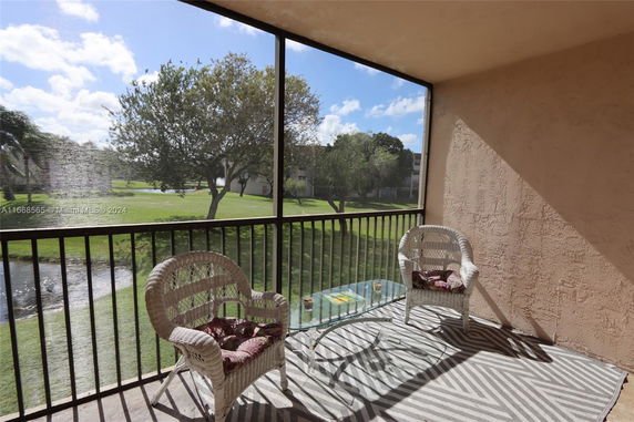 View from a screened balcony with wicker chairs and glass table, overlooking grassy area with trees.
