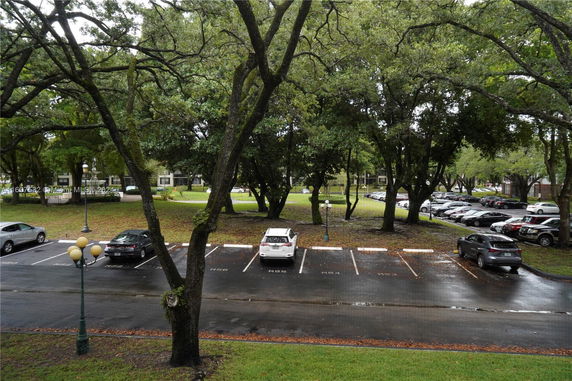 Outdoor parking area with several cars parked and trees surrounding the space.