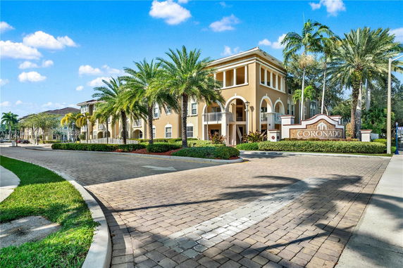 Front view of a multi-story residential building with palm trees and an entrance sign.