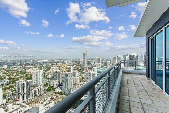 Panoramic view from a high-rise balcony overlooking a cityscape with skyscrapers under a blue sky with clouds.