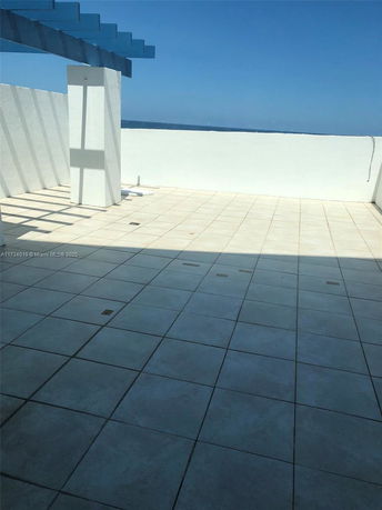 Tiled rooftop area with a white wall and partial blue pergola structure.