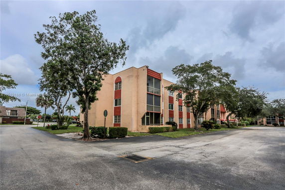 Front view of a multi-story residential building with trees and a parking lot.