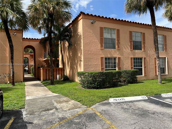 Front view of a two-story building with arched entrance and palm trees.