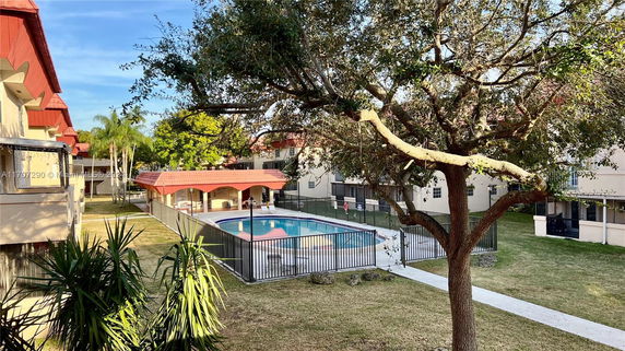 Outdoor swimming pool area with surrounding buildings and a tree.