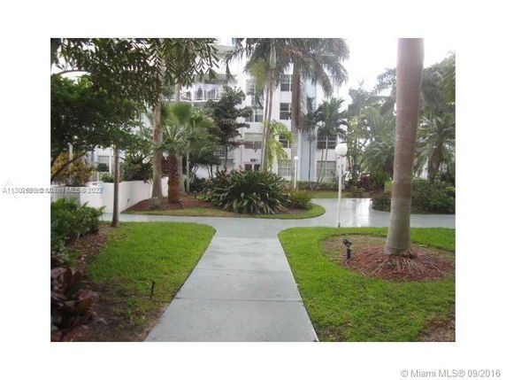View of garden walkway leading to a multi-story building with palm trees.