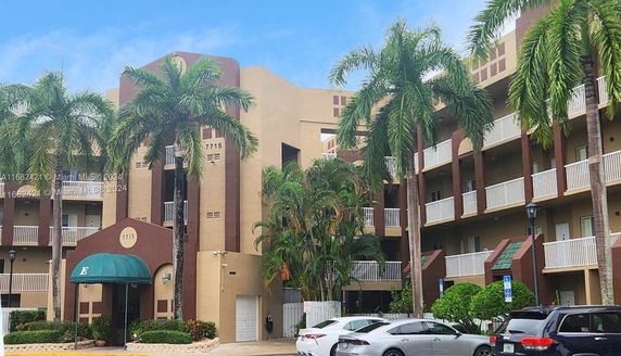 Front view of a multi-story residential building with balconies and palm trees.