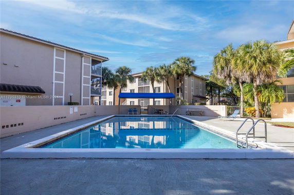 Outdoor swimming pool area surrounded by residential buildings and palm trees.