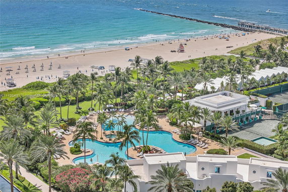 Panoramic view of a beachside area with a swimming pool, trees, and buildings.