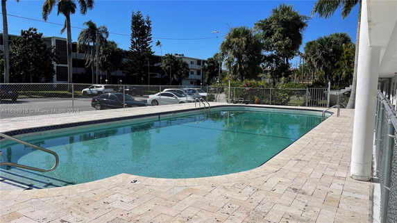Outdoor swimming pool area with surrounding fence and nearby buildings.