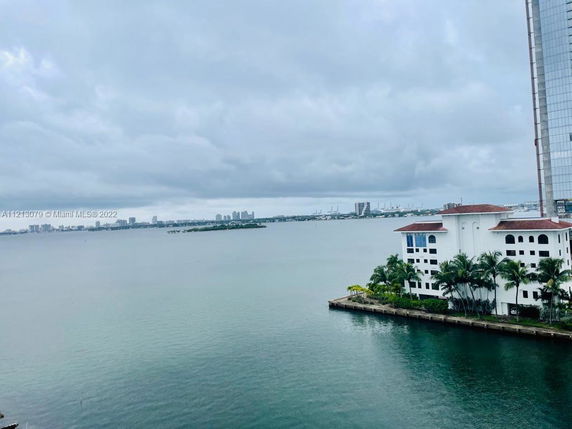 Wide view of a waterfront with buildings in the distance under a cloudy sky.