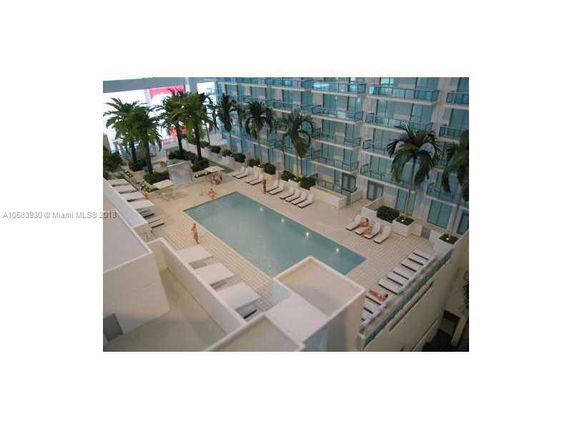 Rooftop view of a modern building with a swimming pool surrounded by lounge chairs and palm trees.