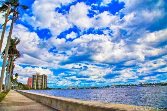 View of high-rise buildings across a body of water with a bridge under a partly cloudy sky.