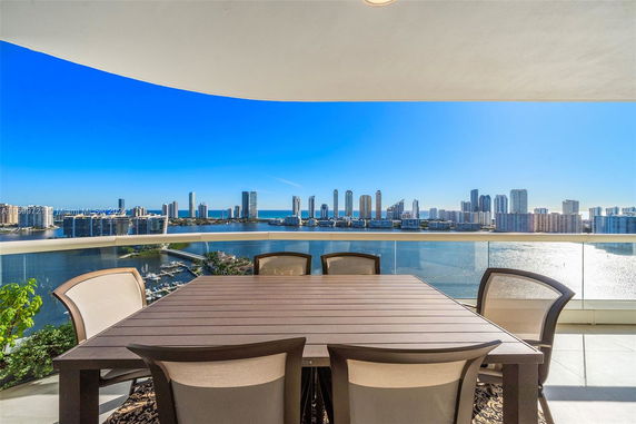Panoramic view from a balcony with seating area overlooking a city skyline and waterfront.