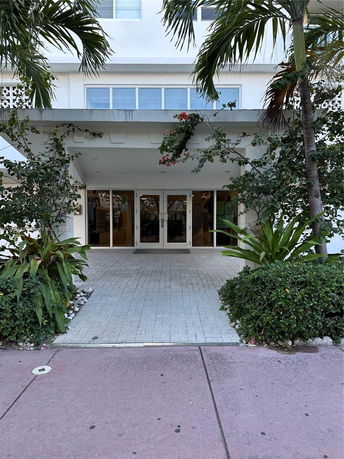 Front view of a building entrance with glass doors and surrounding greenery.