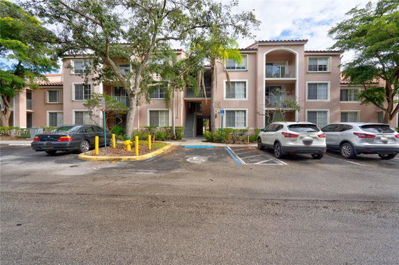 Front view of a three-story apartment building with balconies and surrounding parking area.