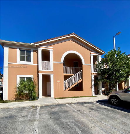 Front view of a two-story building with stucco exterior and an arch over the stairway.