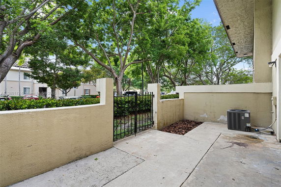 Outdoor area with concrete flooring and a metal gate, adjacent to a residential building, surrounded by trees.