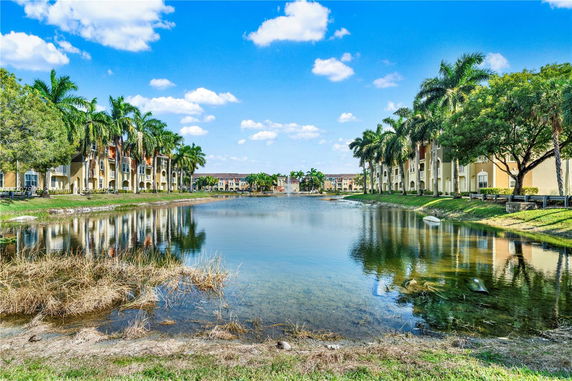 View of multiple residential buildings around a pond with palm trees lining the area.