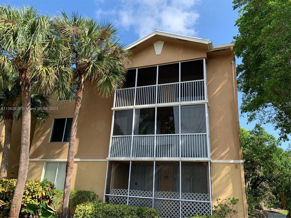 Front view of a multi-story building with screened balconies and palms nearby.