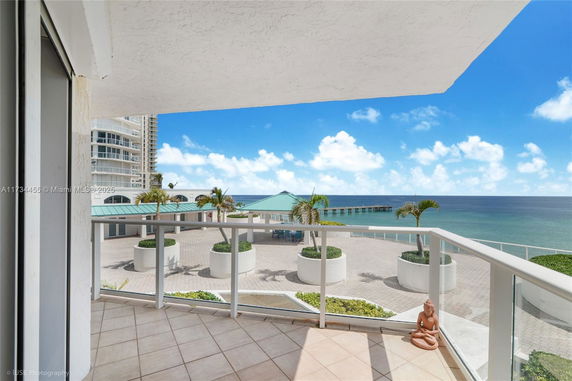 View from a balcony overlooking the ocean and pool area of a building.
