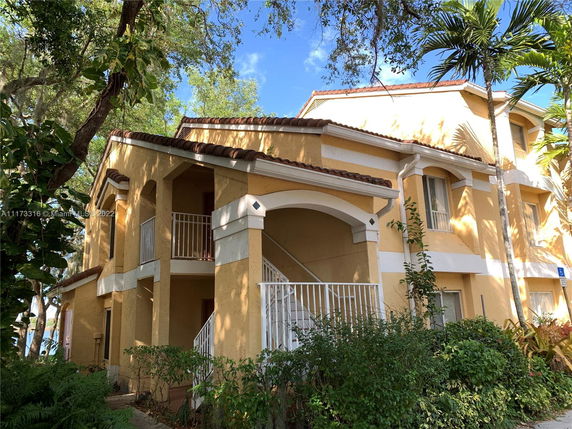 Front view of a two-story yellow house with white railings and a tiled roof.