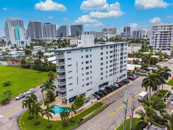 Front view of a mid-rise apartment building with parking area and swimming pool.