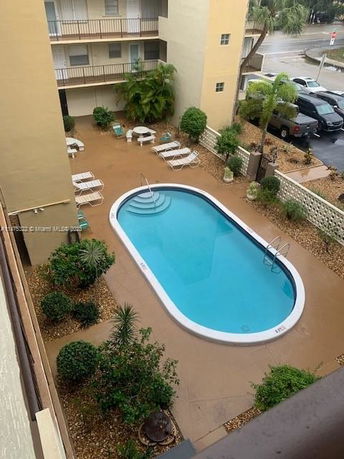 Aerial view of an outdoor swimming pool surrounded by a seating area and adjacent to a multi-story building.