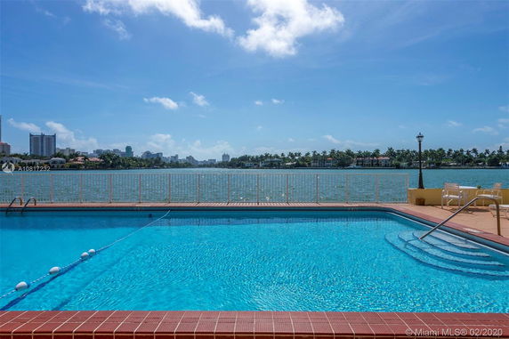 Outdoor swimming pool with a view of a body of water and city skyline in the background.