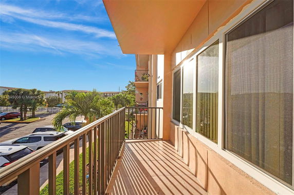 Balcony view overlooking a parking area and palm trees outside an apartment building.