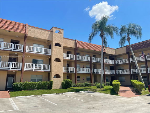 Front view of a three-story residential building with balconies and parking area.