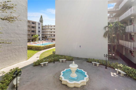 Outdoor swimming pool area surrounded by apartment buildings with a central decorative fountain.