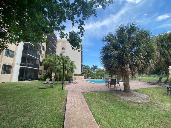View of a multi-story apartment building with balconies and an outdoor swimming pool area surrounded by palm trees and lounge chairs.