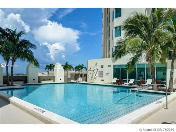 Rooftop with a swimming pool and palm trees adjacent to a multi-story building.