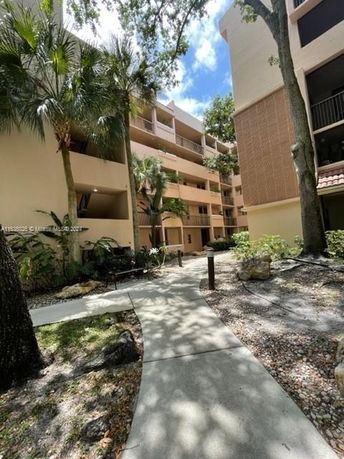 Front view of a multi-story apartment building with balconies and surrounding trees.