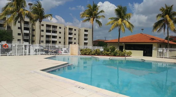 Outdoor swimming pool area with palm trees and adjacent building.