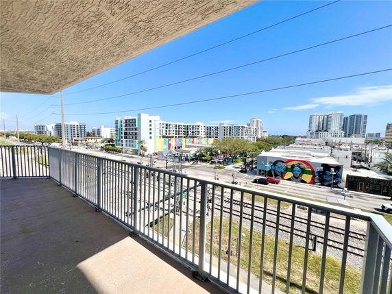 View from a balcony overlooking a cityscape with modern buildings and a mural on a wall.
