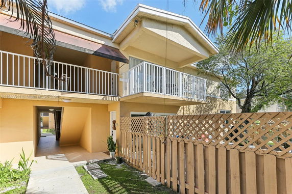 Front view of a two-story apartment building with balconies and a wooden fence.