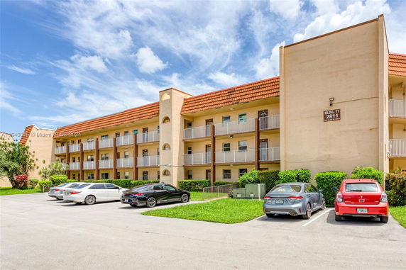 Front view of a multi-story apartment building with balconies and parking area.