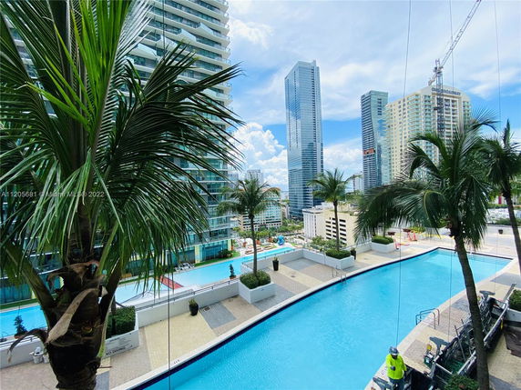 View of a high-rise building with balconies and a swimming pool in the foreground, surrounded by other tall buildings.