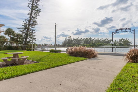 View of a waterfront area with a grassy lawn, pathway, bench, and water taxi sign.