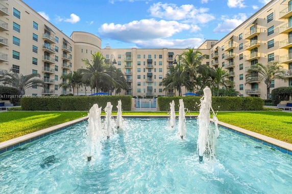 Front view of a multi-story apartment building with balconies and water fountains in the foreground.