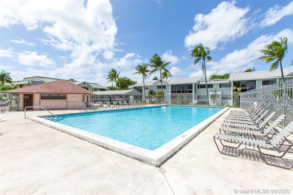 Outdoor swimming pool area with surrounding sunbeds and nearby buildings.
