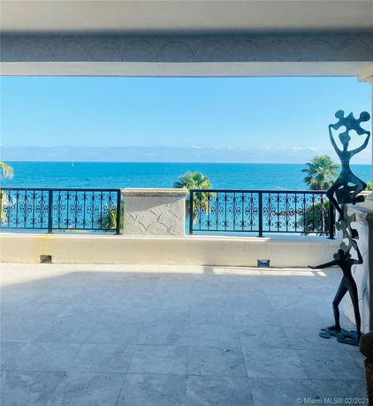 Panoramic view from a building showing a balcony with decorative railings and ocean in the background.