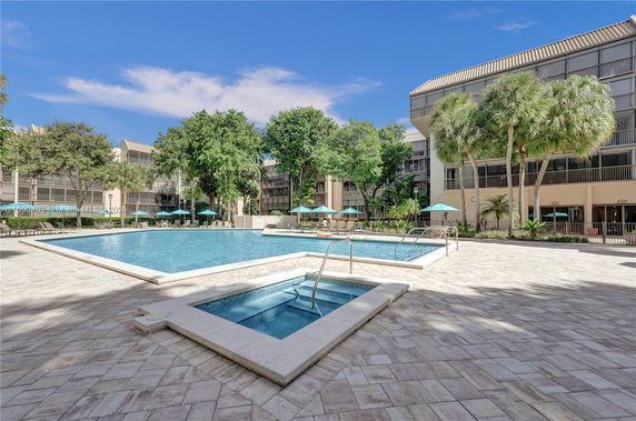 Outdoor swimming pool area surrounded by buildings with tropical landscaping.
