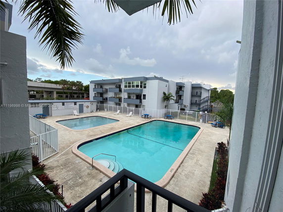 Outdoor area with a swimming pool surrounded by a fence and residential buildings.
