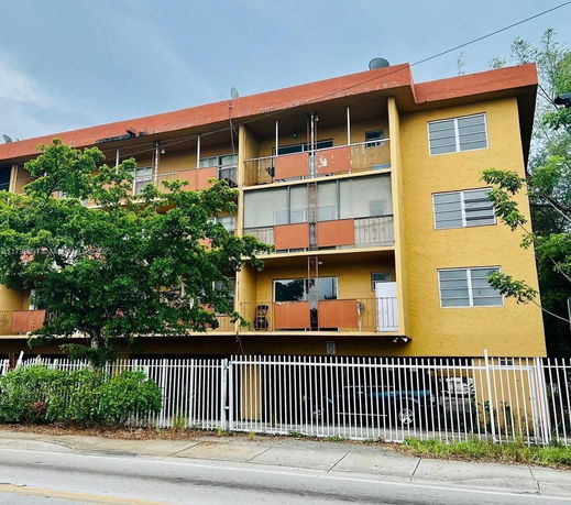Front view of a multi-story apartment building with balconies and a gated entrance.