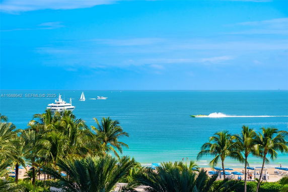 View of a coastal area with several boats on the sea, palm trees, and a beach with umbrellas.